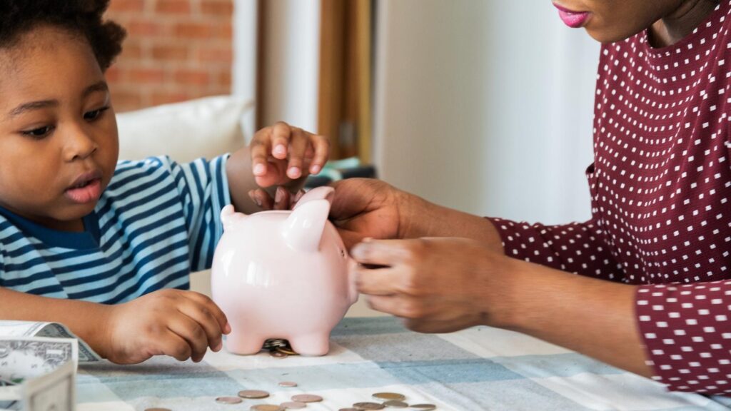 Child and adult saving money in a piggy bank Learning about saving finances and money management Coins and cash on the table Family financial education African family at home