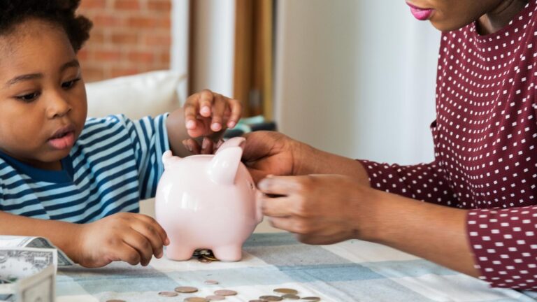 Child and adult saving money in a piggy bank Learning about saving finances and money management Coins and cash on the table Family financial education African family at home