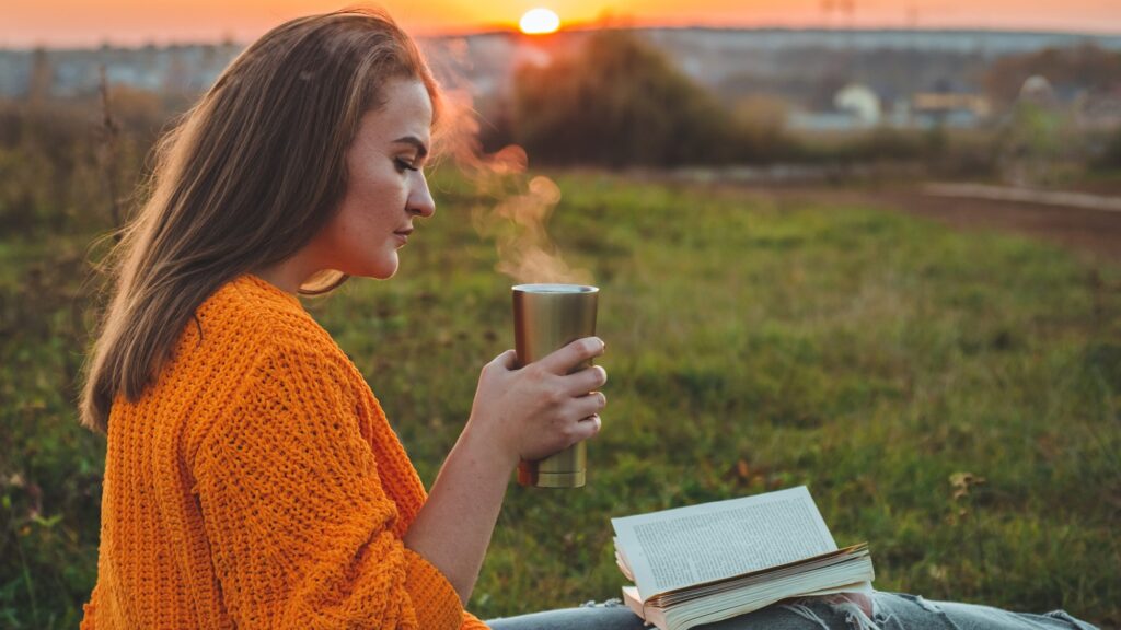 The concept of lifestyle and family outdoor recreation in autumn. woman read books on plaid with a thermo cup. Autumn. Sunset. Cozy