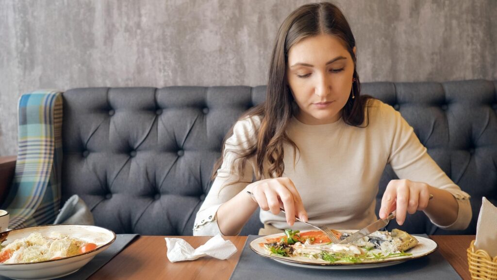 Young woman eating dinner in the restaurant. Cutting fish steak with knife and fork. Healthy eating and diet concept.