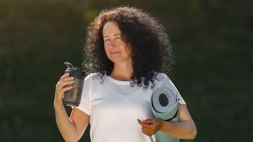 Mature lady training in a summer park. Brunette doing yoga. Old woman in a sports clothes.