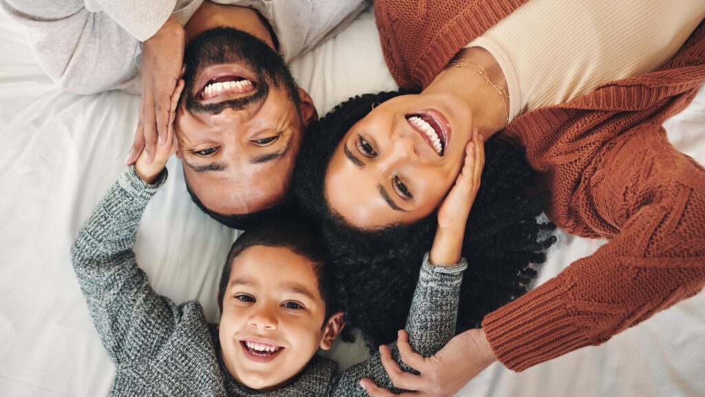 Family laughing and top view portrait on bed in bedroom bonding and care in home Love smile and happy mother comic father and funny boy child playing having fun and enjoying joke time together