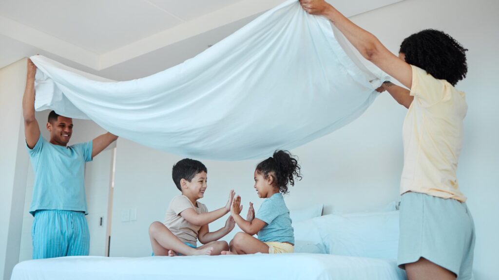 Children play and family with blanket in bedroom bonding and smile together Interracial kids game and father and mother at bed with sheet for patty cake happy and enjoying quality time in house