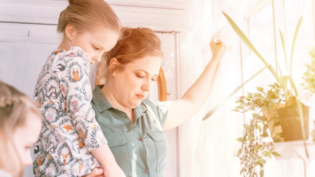 Happy family mother with kids daughters girls have fun in suburb countryside home life on sunny spring day candid mom and children standing by window with plant people love and care moment flare
