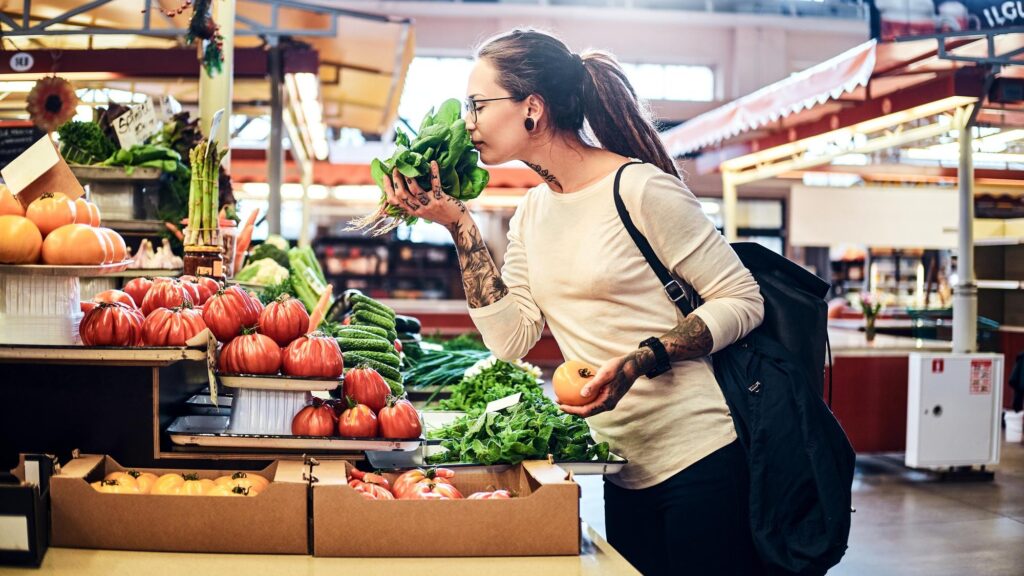Young attractive woman with tattooes choosing fresh salad at vegetable market.