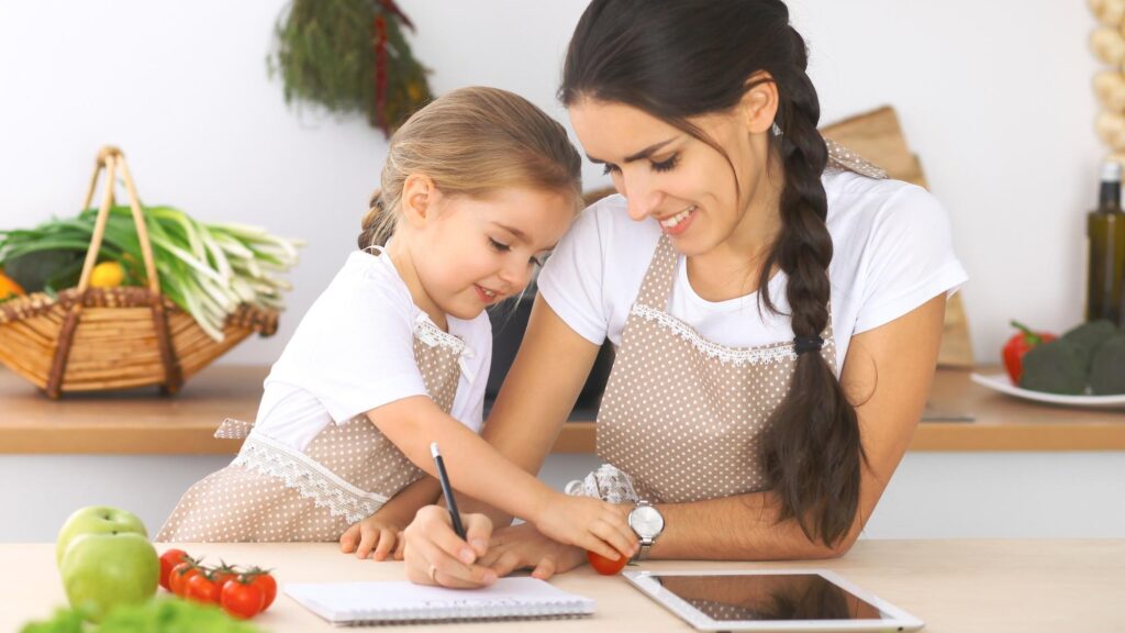 Happy family in the kitchen Mother and child daughter make menue for cooking tasty breakfest in the kitchen Little helper is ready for houshold job
