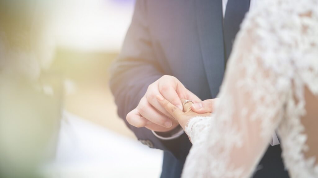 Closed up of groom put wedding diamond ring on bride finger in wedding ceremony to commit marriage.