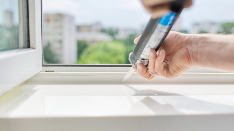 A worker with a construction syringe fills seam between sill and window with silicone sealant