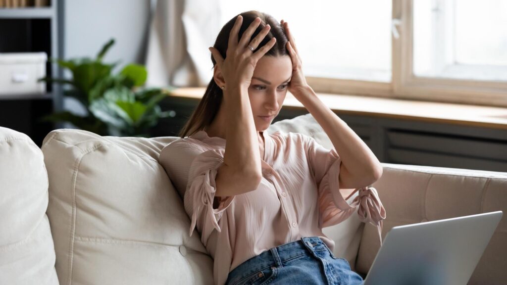 Nervous frustrated young woman holding head in hands feeling shocked about bad news looking at computer screen Stressed worried lady reading bank loan debt notification dismissal notice