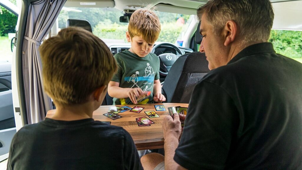 A family playing a game of Uno int the back of camper van while taking a road trip holiday. Please use this image and provide a link back to https://www.cruiseamerica.com