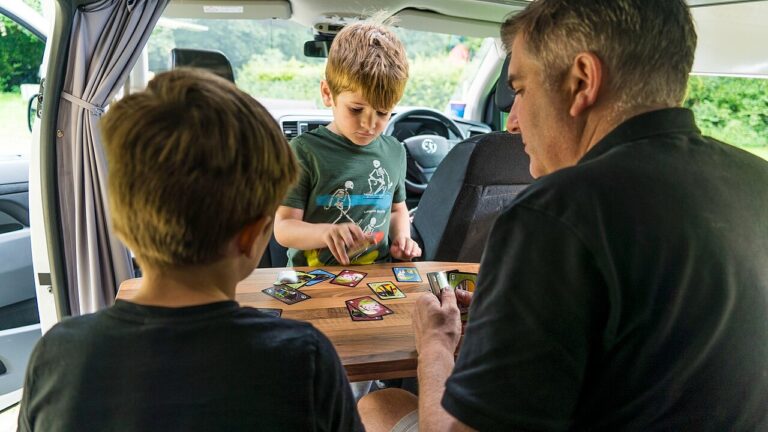 A family playing a game of Uno int the back of camper van while taking a road trip holiday. Please use this image and provide a link back to https://www.cruiseamerica.com