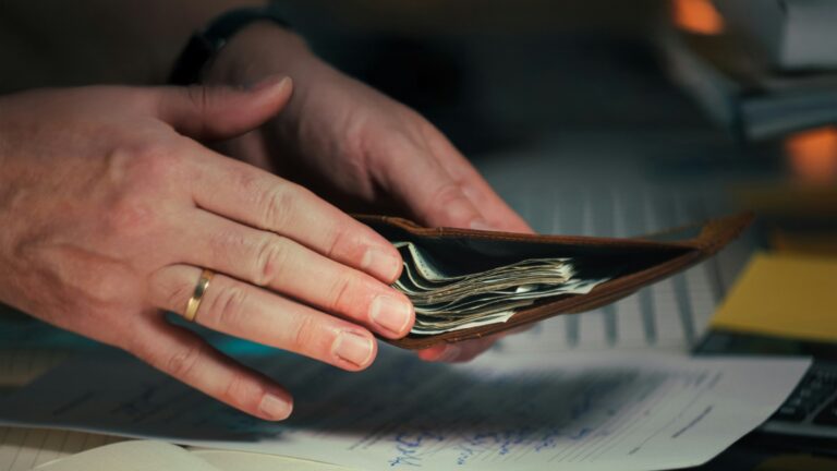 Hands holding cash in a wallet over papers.