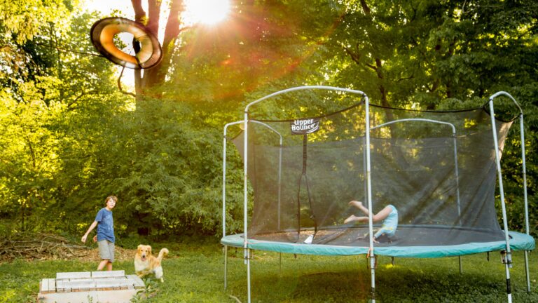 two children playing on a trampoline in a yard