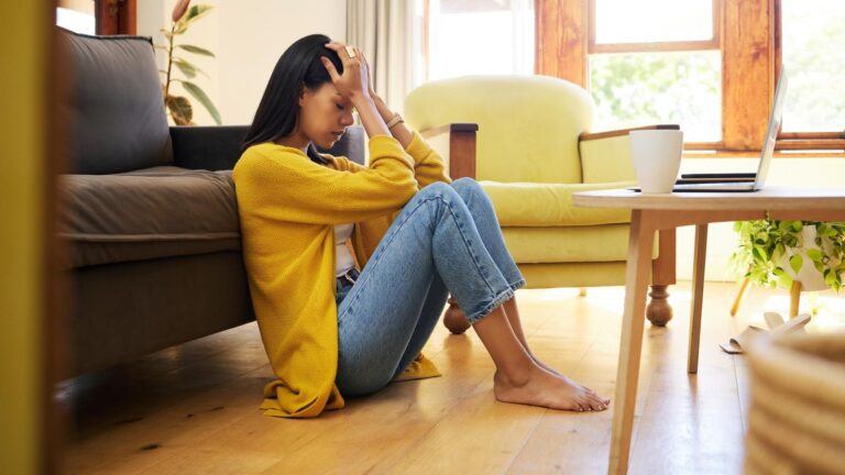 Stressed woman depression and lonely in the living room sitting on the floor at home Young sad female suffering from mental health issues and anxiety or headache in apartment or house