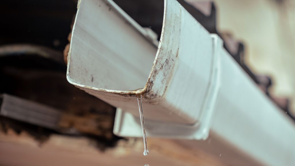 Detailed shot of rainwater droplets falling from a house gutter, emphasizing water flow.