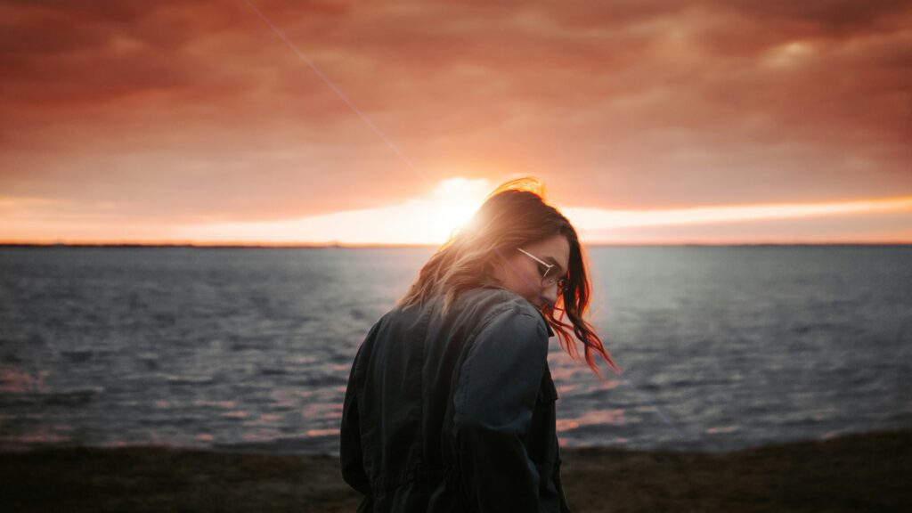 woman in black jacket standing on beach during sunset
