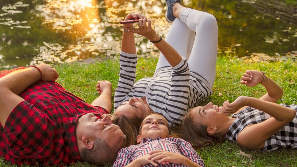 Happy family together laying on green grass and take a selfie with mobile phone