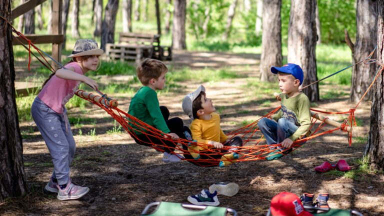 a group of kids sitting in a hammock in the woods