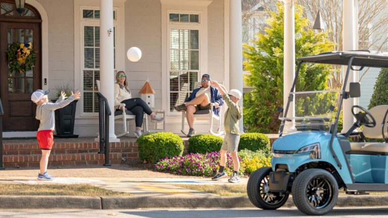 Two boys play ball near a golf cart and adults.