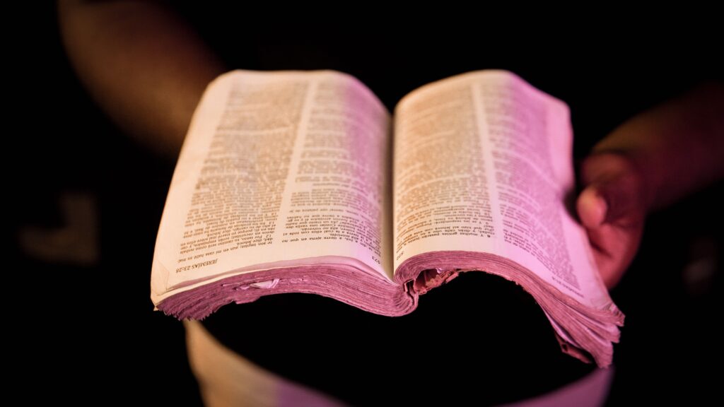 An open Bible held in hands with dramatic lighting, creating a serene atmosphere.