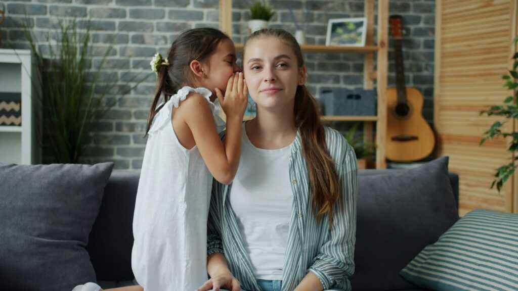 Girl whispers a secret into a woman's ear