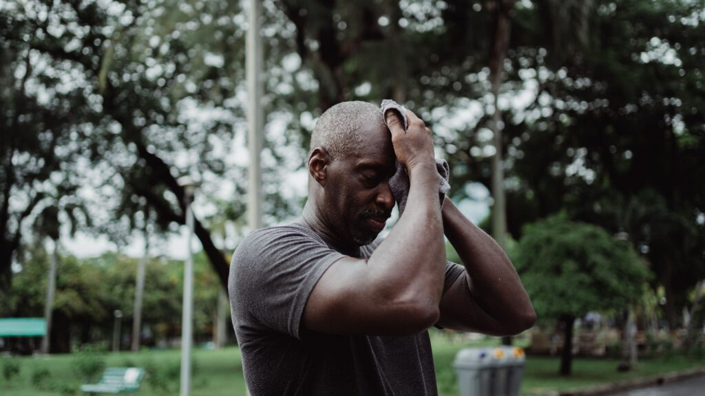 Black man wipes sweat with towel after an intensive workout outdoors.
