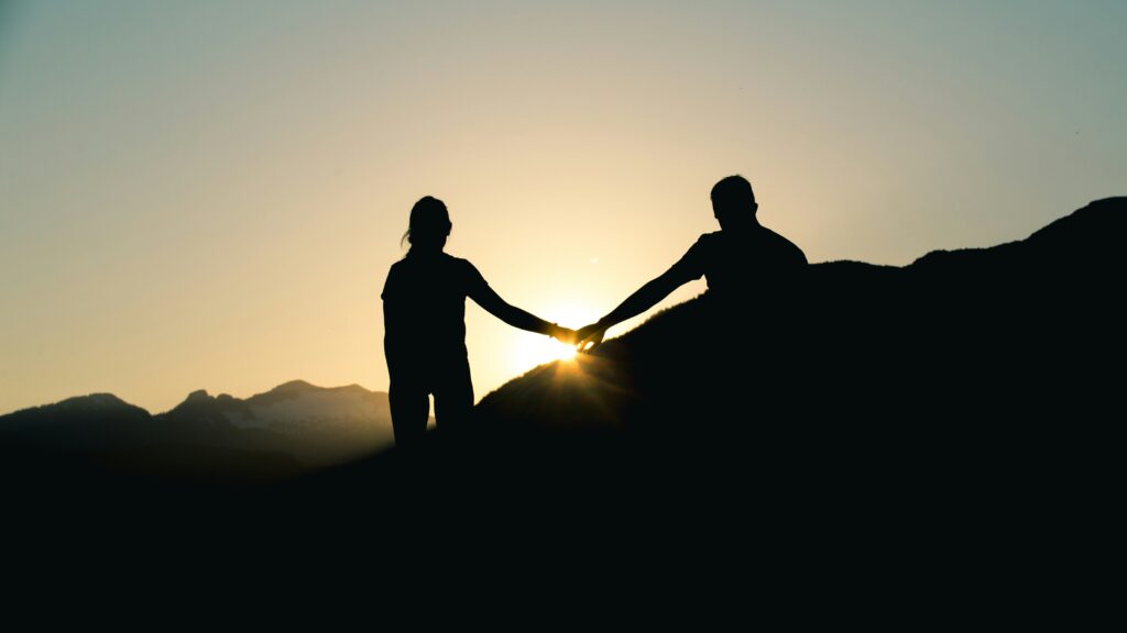 silhouette of man and woman holding hands while walking under gray sky during daytime