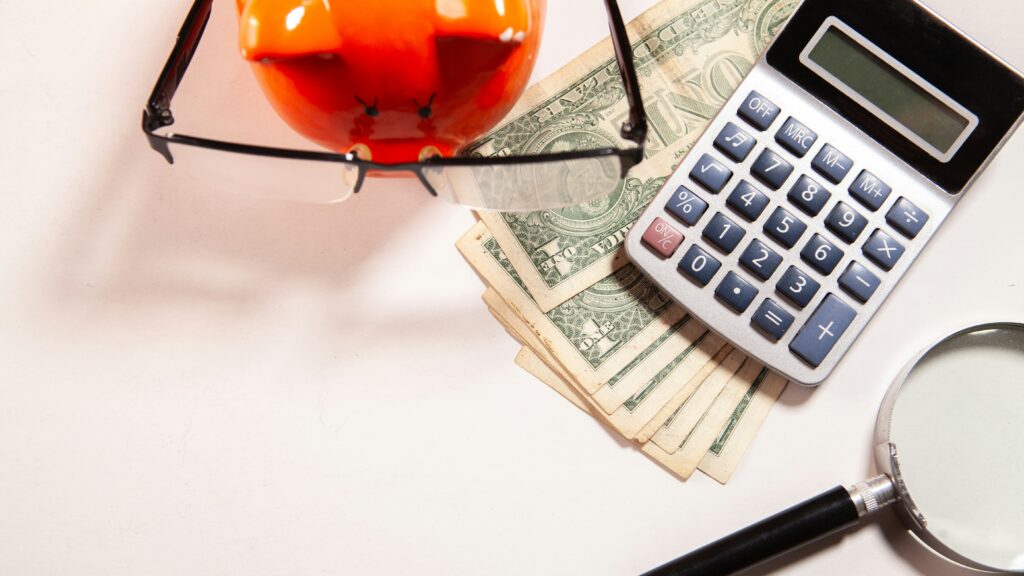 Calculator, magnifying glass, glasses, and money on white surface.