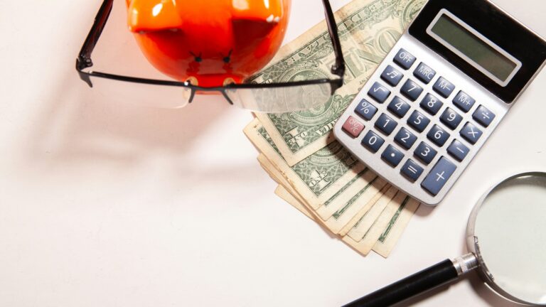 Calculator, magnifying glass, glasses, and money on white surface.