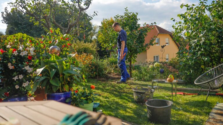 Man walks through a lush garden with a house.