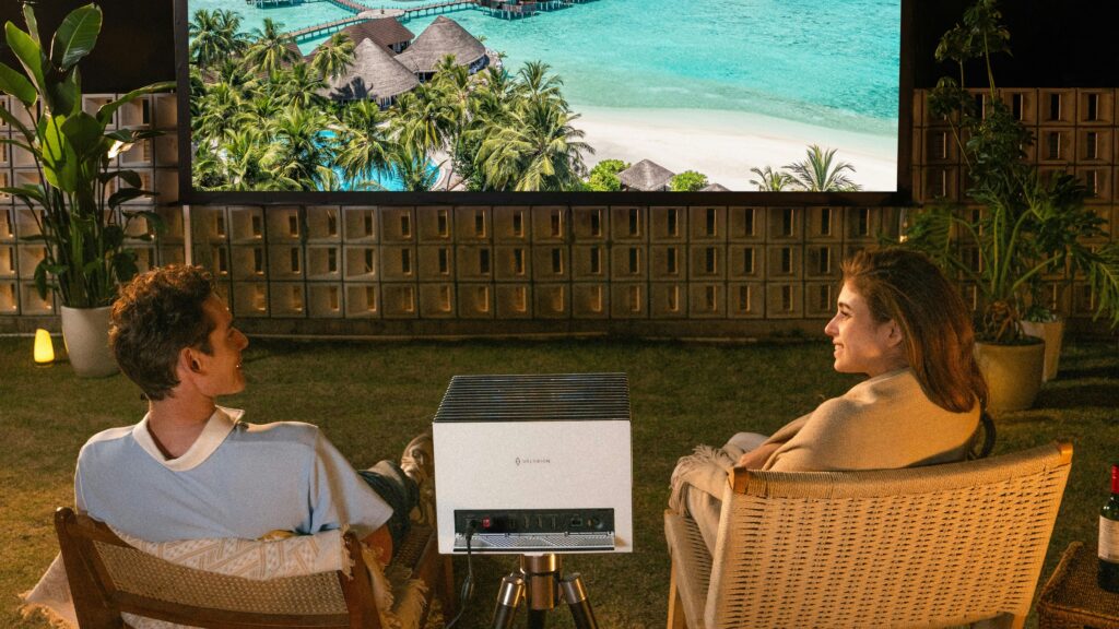 Couple watches movie on outdoor projector screen at night.