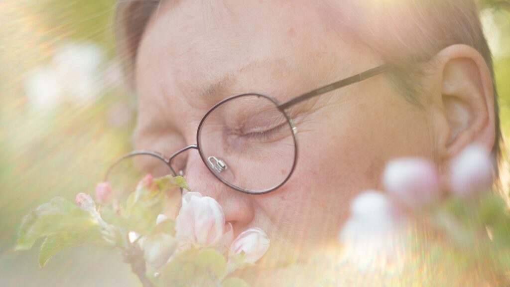 a woman with glasses is smelling a flower