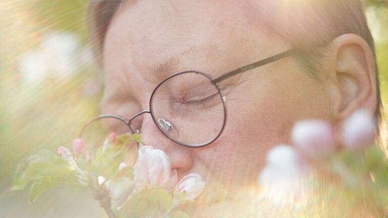 a woman with glasses is smelling a flower