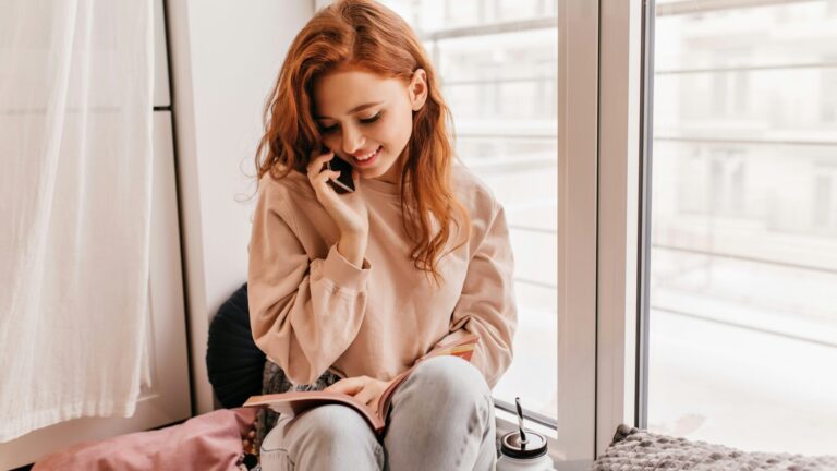 a woman sitting on a window sill talking on a cell phone