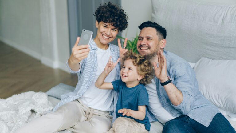a man, woman and child sitting on a bed taking a selfie