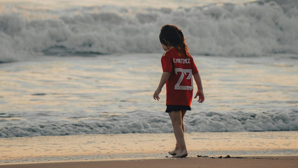 a little girl standing on top of a beach next to the ocean