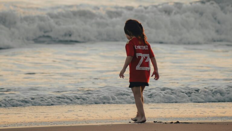 a little girl standing on top of a beach next to the ocean