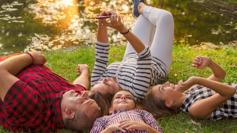 Happy family together laying on green grass and take a selfie with mobile phone