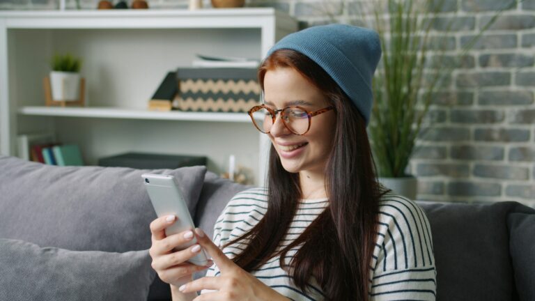 Young woman wearing a beanie and glasses using phone
