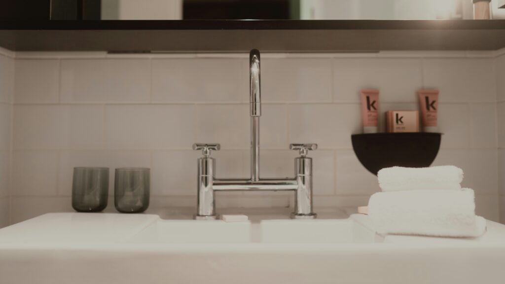 A modern bathroom sink with chrome faucet, glasses, and towels