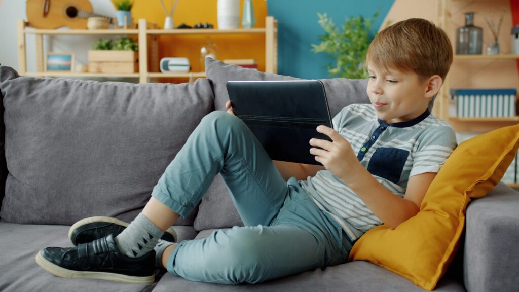 Young boy watches tablet while relaxing on couch