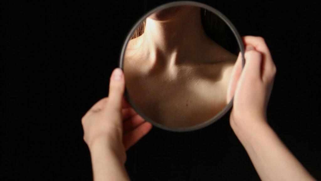 Hands hold a mirror reflecting a person's neck