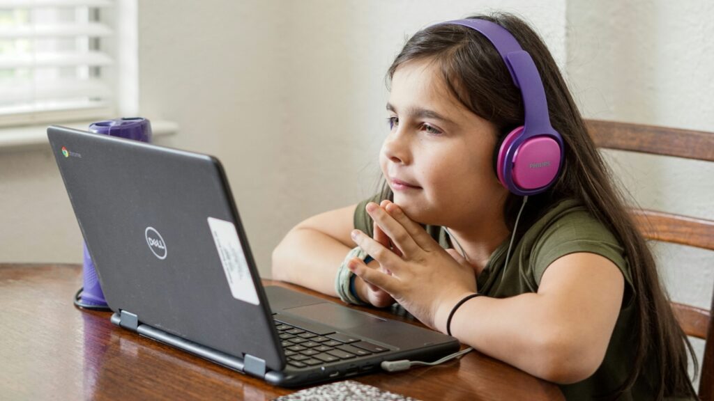 a little girl sitting at a table with a laptop