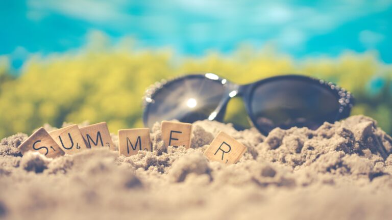 Sandy beach scene with sunglasses and 'summer' spelled in letter tiles, capturing vacation vibes.