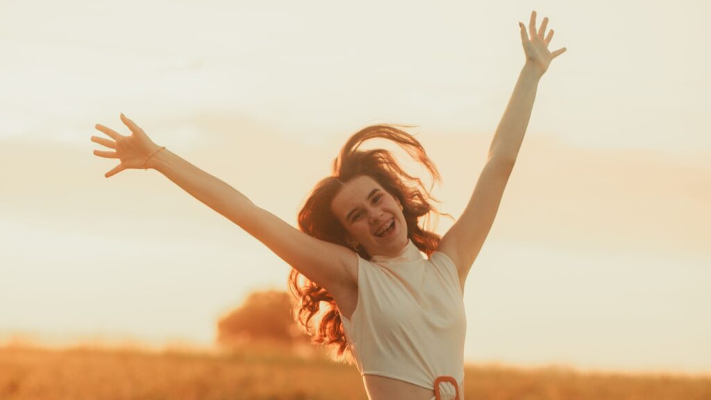 Happy woman in a floral dress leaping joyfully in a sunlit field at sunset.