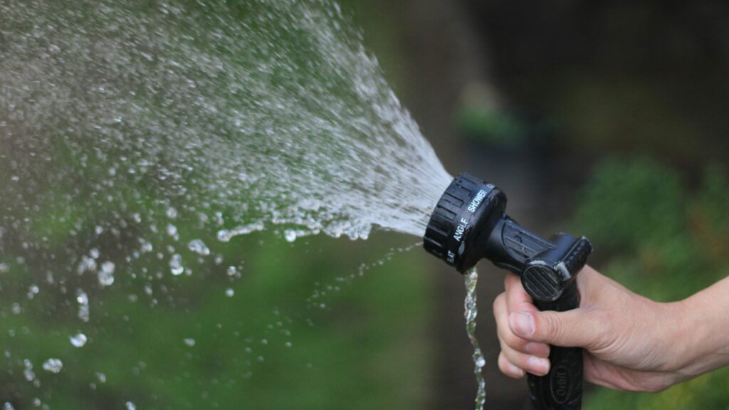 a hand holding a water hose spraying water