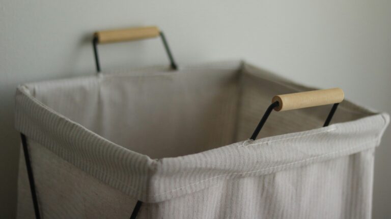 An empty, light-colored laundry hamper with wooden handles