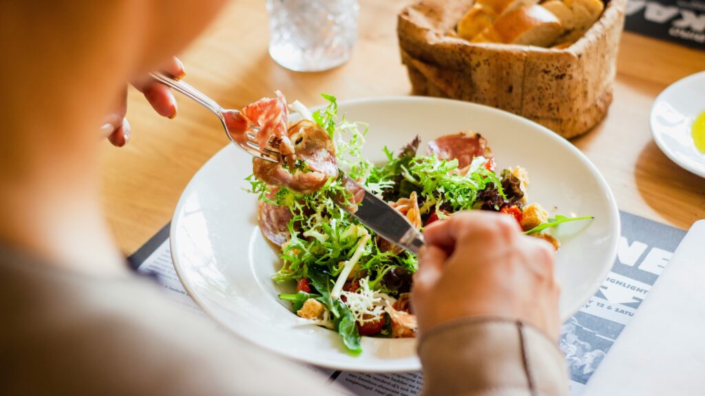 A person eating a salad with cured meat and croutons from a white plate