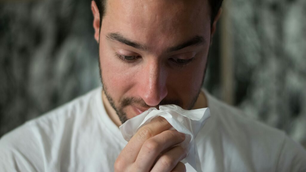 sick man blowing nose into tissue