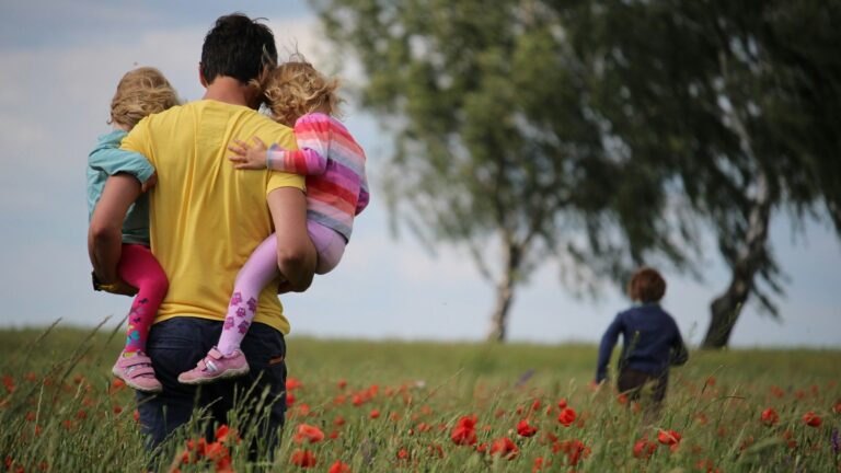 man carrying to girls on field of red petaled flower